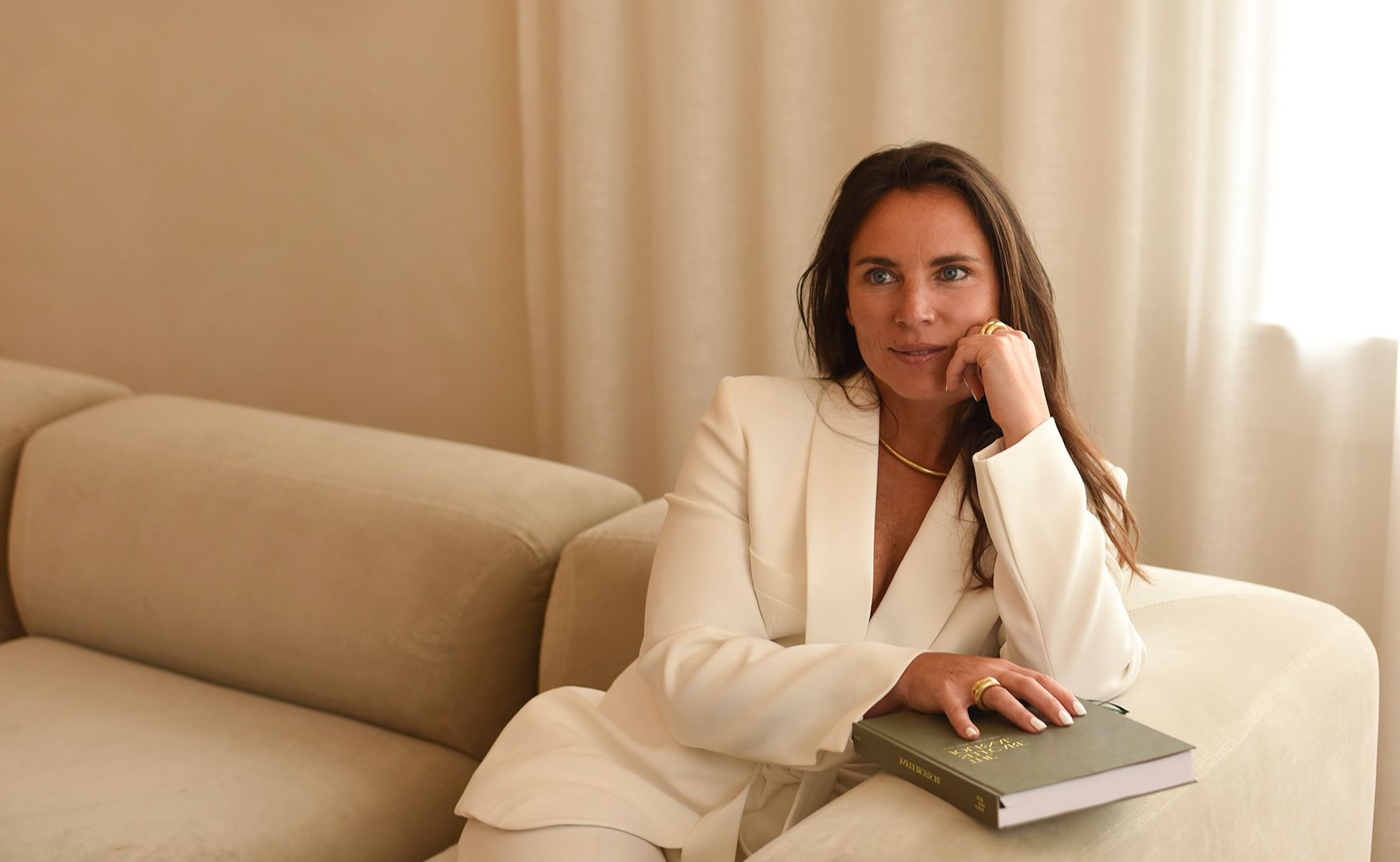Hanneke Peeters zittend op een bank, licht voorovergebogen met een hand op een groen boek